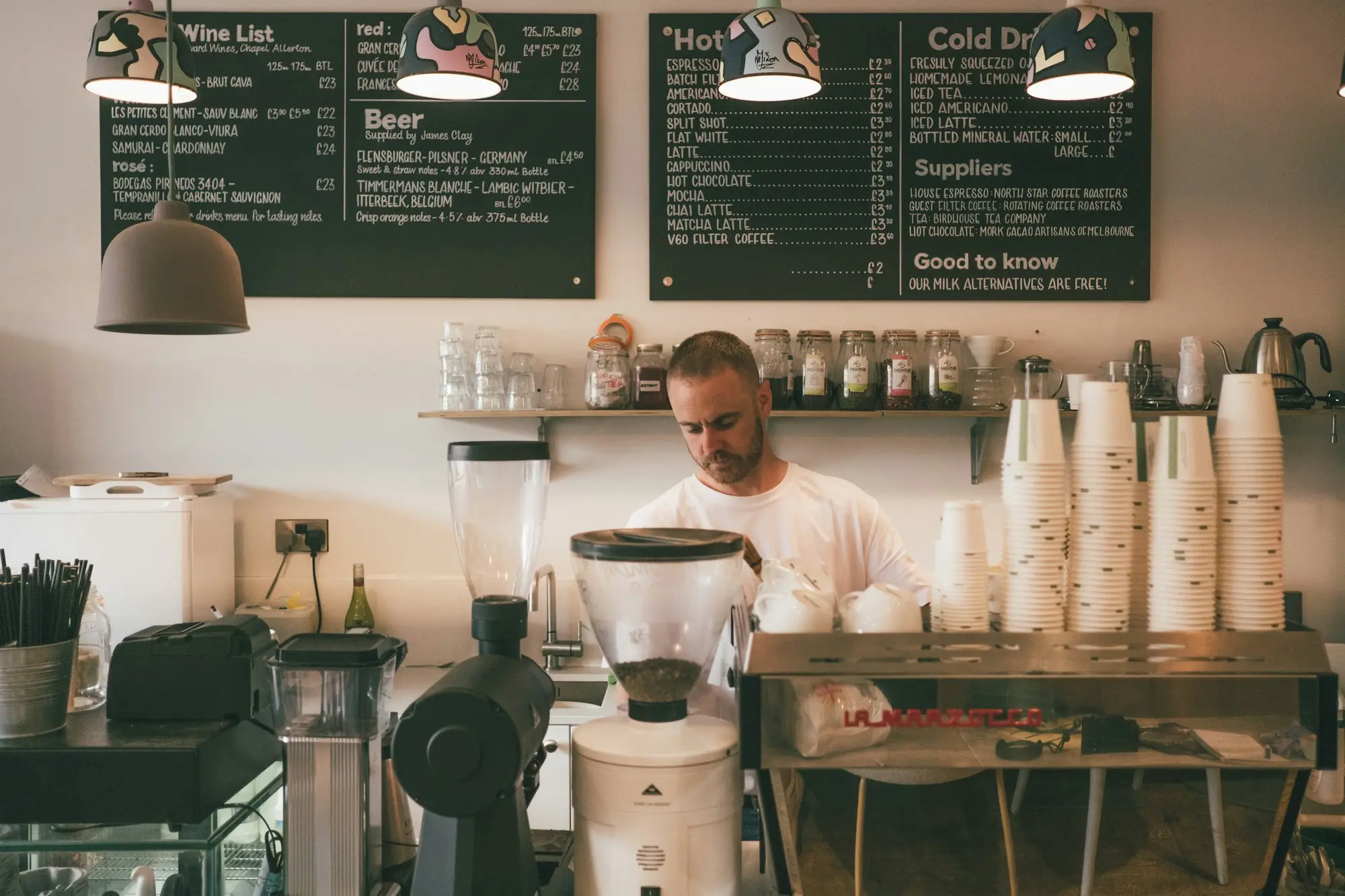Café owner behind the coffee counter with chalkboard menus, running the business as usual while it's up for sale